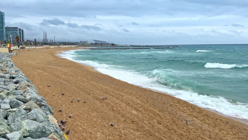 Waves breaking on the sand at Somorrostro beach with the Port Olímpic in the background in Barcelona, Spain. Copy space