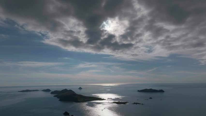 Dramatic aerial shot of the Great Blasket Island in Ireland, featuring sun rays breaking through thick clouds over the Atlantic Ocean.