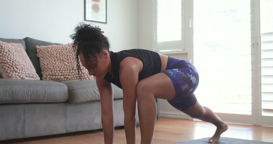 African woman starting low lunge, flowing into twist on home mat, in sportswear for workout. Yoga, fitness, flow, rotation, daylight, hardwood, apartment