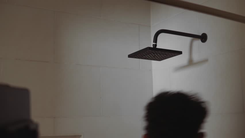 Masculine figure engaged in a daily hygiene ritual, washing hair under a stream of water in a bathroom for personal cleanliness and refreshment