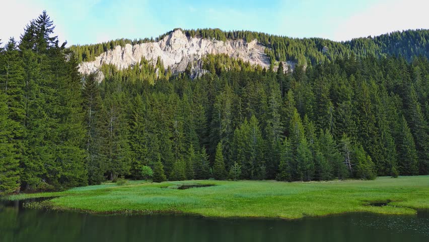 A lake reflects sunlight, against blue sky and mountain ranges and villages