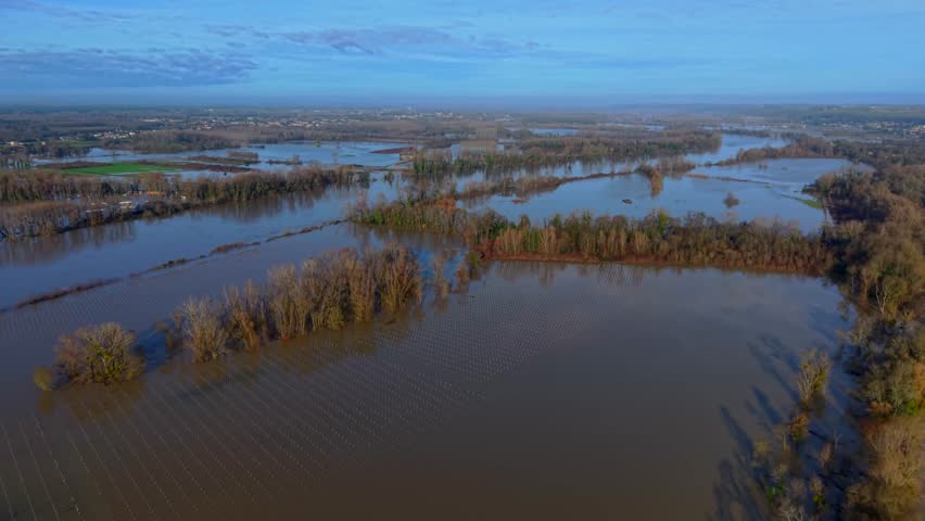 Aerial view of flooded vineyards reflecting the sky, with trees emerging from the water, creating a stark contrast against the submerged landscape, Rions, France.