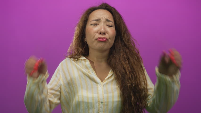 Young caucasian woman rubbing her eyes and puffing lips in purple studio wearing yellow striped shirt and red nails; pouty sadness.
