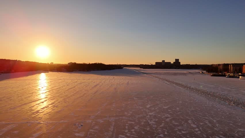 Beautiful sunset over the frozen lake Mälaren in Stockholm Sweden, people on the ice, broken ice path for the boats, kungsholmen area, aerial view,