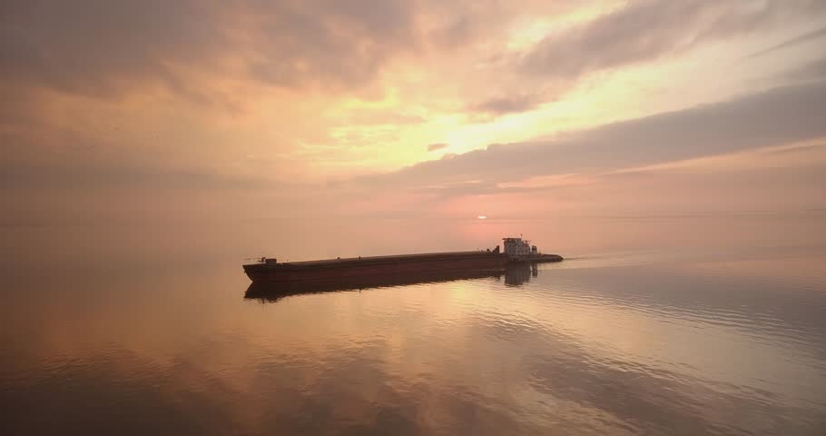 Flying over the calm water of the river during a beautiful dramatic sunset with an orange sky, peace and quiet, a large ship
