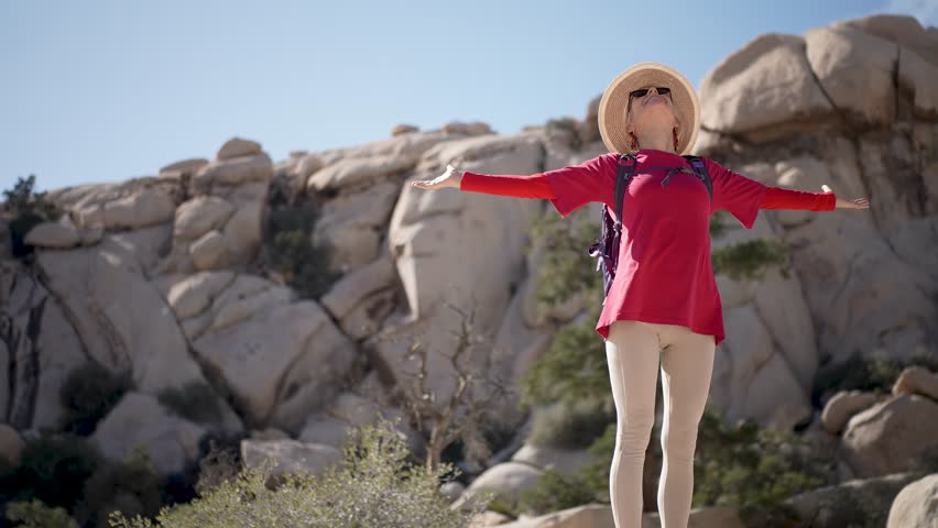 A mature woman hikes and climbs rocks in Joshua Tree National Park, embracing the beauty of nature and the California landscape