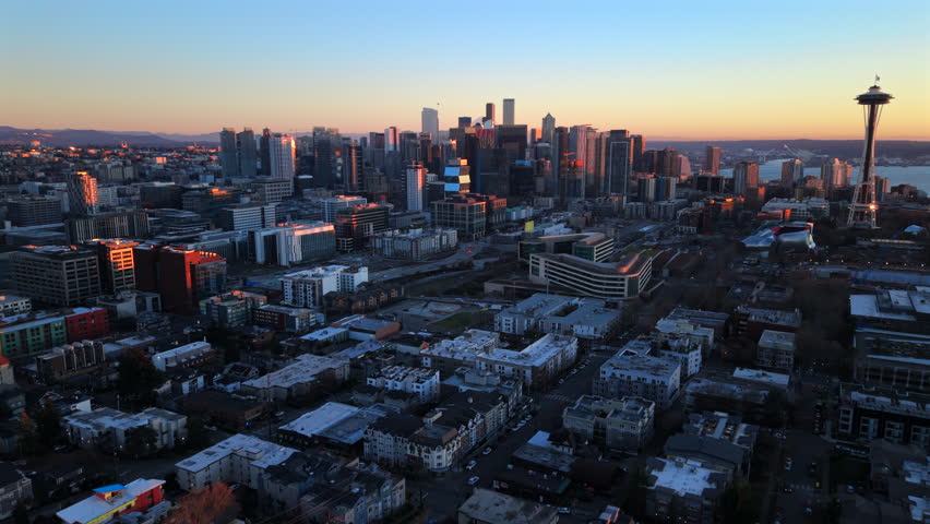 Seattle Washington, 01.18.2026. Aerial view of Seattle Washington skyline with Space Needle and dense downtown blocks at sunset, warm evening light highlighting modern towers, calm coastal atmosphere.