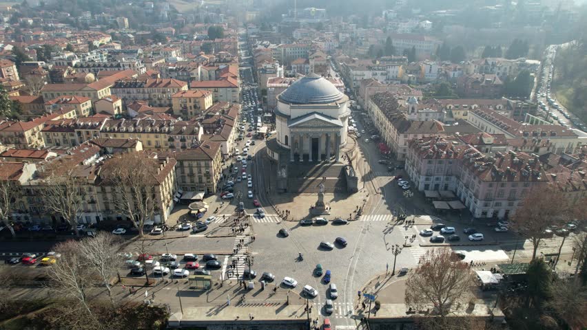 Aerial drone shot shows the neoclassical Gran Madre di Dio church and surrounding city blocks with traffic in Turin, Italy, historical landmark architecture, urban panoramic scene.