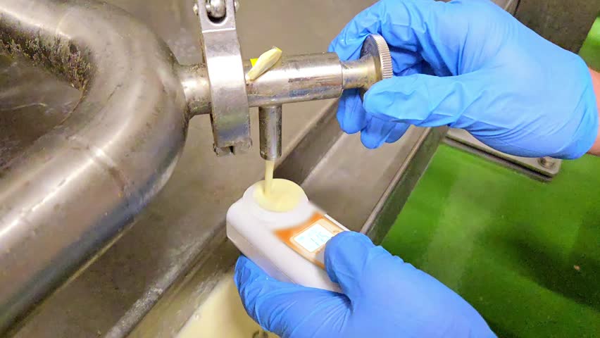 Close-up of worker in blue gloves measuring the Brix level of fresh soy milk using a digital refractometer at a production line.