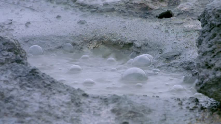 Close up view of a boiling mud pot in a geothermal area, with steam and gas bubbles rising