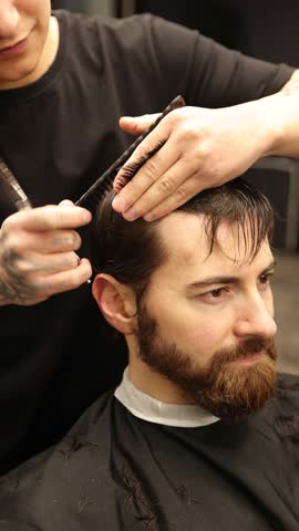 Barber cutting man's hair with scissors in salon, closeup