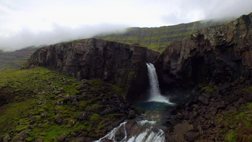Majestic waterfall cascading down basalt cliffs into a turquoise pool in a foggy Iceland landscape