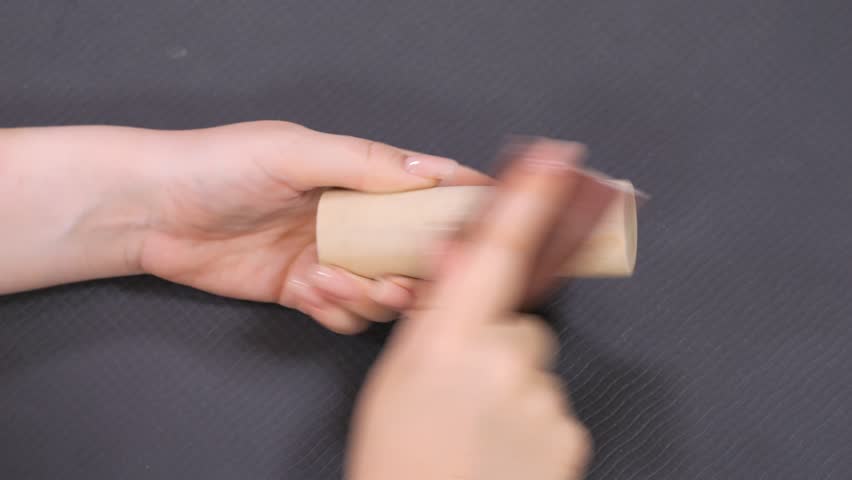 Person is holding a piece of wood and sanding it. The wood is brown and has a rough texture