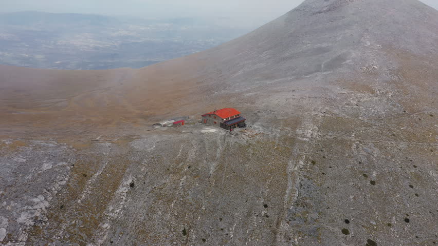 Slow panning drone shot of Giosos Apostolidis Refuge surrounded by rugged mountain terrain in Mount Olympus, Greece
