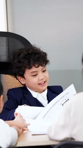 A young boy wearing a suit discusses documents during a corporate meeting in an office