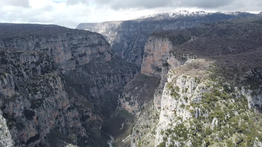 A slow cinematic drone pan to the left, revealing the majestic depths of Vikos Gorge. Highlighting the towering limestone cliffs and rugged wilderness of the Pindus Mountains in Northern Greece.
