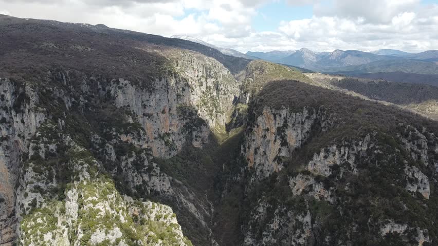 A cinematic wide drone shot capturing the immense scale of Vikos Gorge. Highlighting the towering limestone cliffs and the rugged wilderness of the Pindus Mountains in Northern Greece.