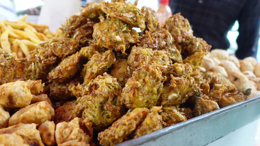 Assorted fried street food on display at local market featuring vegetable fritters and crispy nuggets with french fries