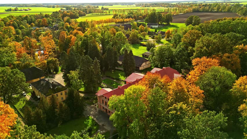 Drone view of a rural European village with red roofs nestled among vibrant autumn trees and farmland