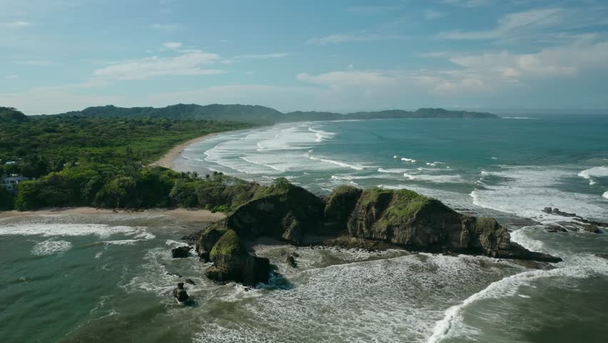 Aerial drone view of rocky headland at Guiones Beach in Nosara, Costa Rica, with waves crashing along the shoreline