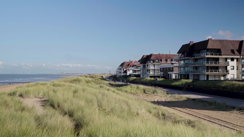 Pan from beach front houses over grass dune to knokke beach belgium