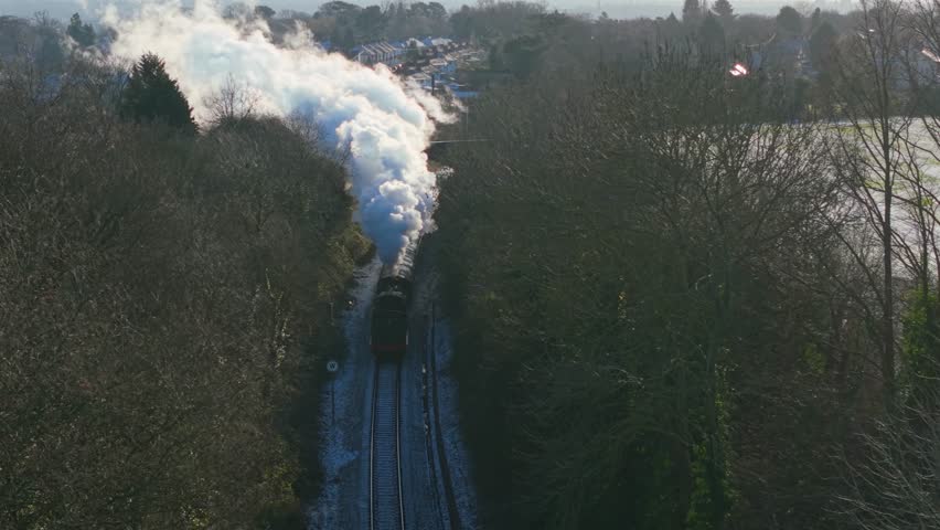 Aerial view retro steam locomotive advancing along railway tracks while releasing massive white steam and smoke. Vintage rail transport moving forward and sending rolling pale vapor clouds across