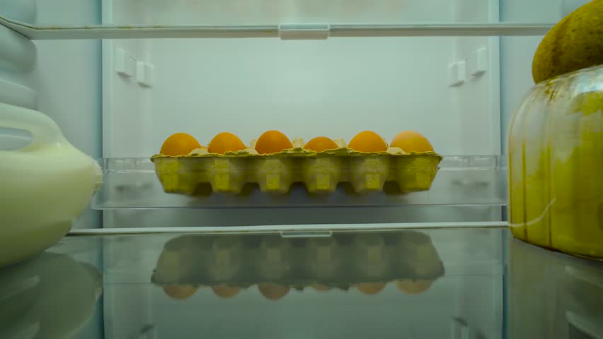 Man opening fridge and staring blankly inside with indifferent expression, view from inside of fridge. Male checking contents while feeling uninterested and passive. Guy standing still and observing