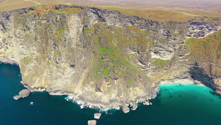 Aerial view of steep limestone cliffs overlooking a turquoise cove and the Arabian Sea at Eftalquot View, Salalah, Oman.