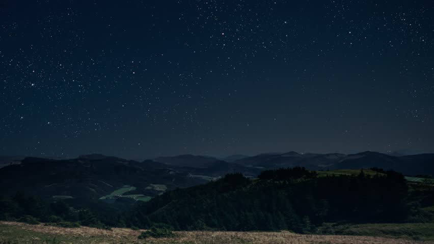  a movement of stars in the night sky with the view of mountains.	