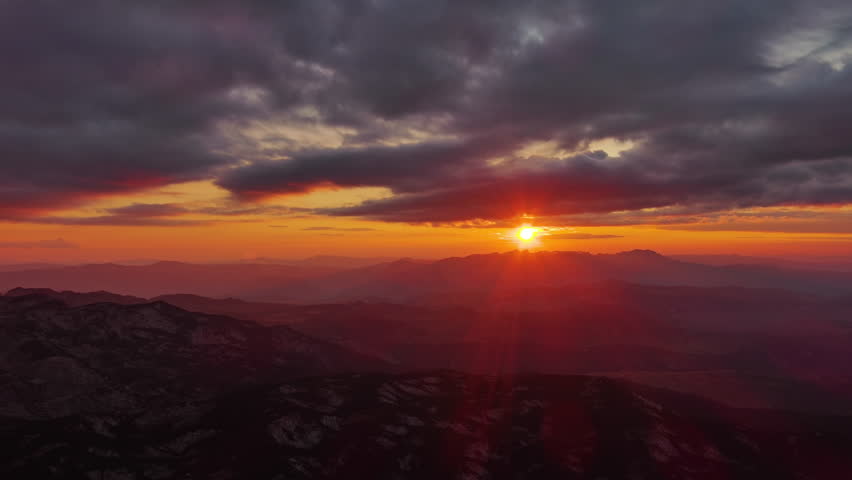 Orange sun setting over mountain with dramatic clouds. Beautiful evening sky at sunset with orange light, aerial view 4k
