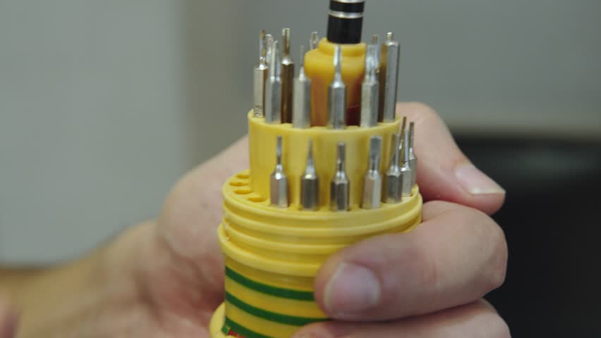 Man arranging interchangeable screwdriver bits in plastic organizer. Person placing metal bits for manual screwdriver into slots of round case. Fine motor skills development, space organization.