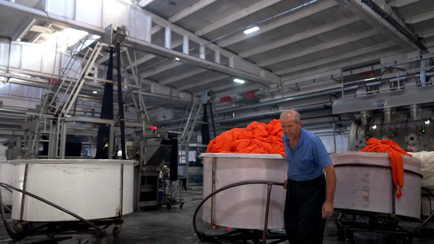 Experienced worker operating within large textile machinery in a factory. Professional industrial footage highlighting human labor, responsibility and large scale textile manufacturing.