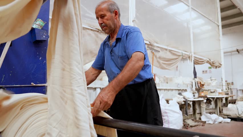 Experienced textile worker manually guiding fabric inside a factory. Footage highlighting human labor, physical effort, attention and quality responsibility in industrial production.