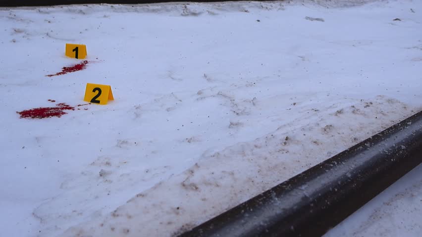 Side angle view of forensic evidence markers and blood stains on snow covered railroad tracks during falling winter snow.