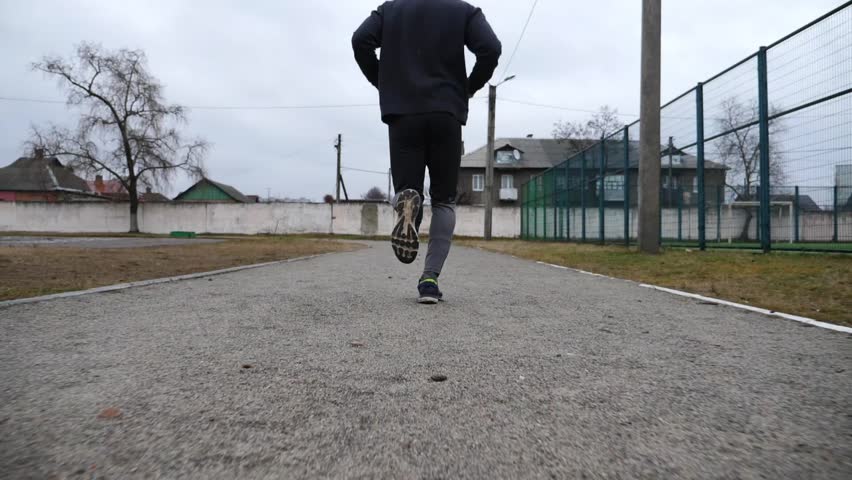 Strong sportsman running at track on school stadium in cloudy day. Young male athlete working out at path on athletic field. Hardy sporty man doing cardio training outdoor. Sportive lifestyle concept