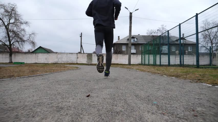 Strong sportsman running at track on school stadium in cloudy day. Young male athlete working out at path on athletic field. Hardy sporty man doing cardio training outdoor. Sportive lifestyle concept