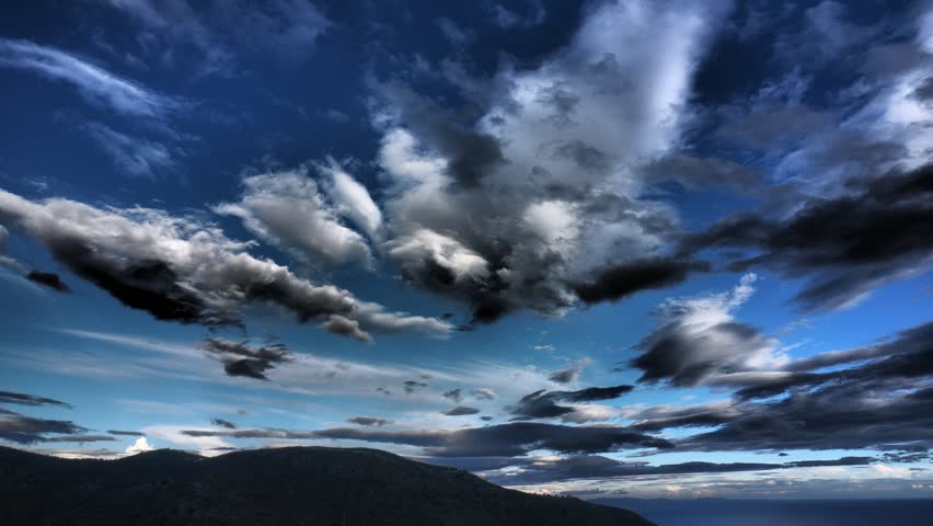 Stylised Ultra high definition 4K timelapse of a dynamic skyscape above Kea Island in the Cyclades, Greece. Fast moving cumulus and stratocumulus clouds drift across the Aegean sky while higher cirrus streaks create layered texture. Alternating sunlight and shadow sweep across the landscape below, producing dramatic contrast and shifting illumination typical of unstable maritime Mediterranean weather conditions.