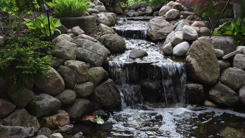 Decorative garden waterfall with stone stream and lush greenery in Ornamental Gardens in Ottawa, Canada.