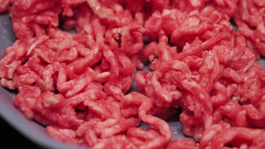 A close-up of fresh ground beef. The cook begins preparing pasta Bolognese and fries the ground beef in a pan.