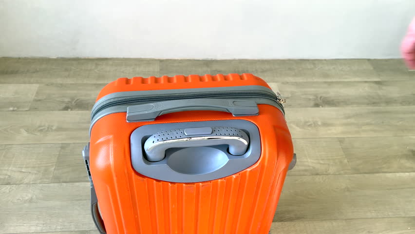 Close-up of a female hand pulling out the retractable handle of an orange travel suitcase