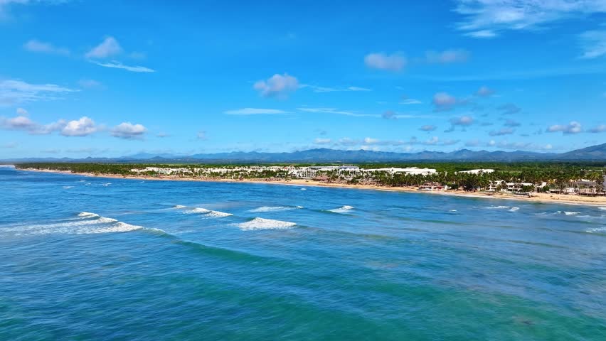 Turquoise water of the Caribbean Sea, big waves, and a clear blue sky. Aerial view. A beautiful tropical resort beach in the Dominican Republic, aerial view. Summer vacation on a picturesque beach.