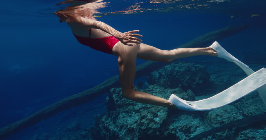 Woman with diving fins swims in transparent blue water.