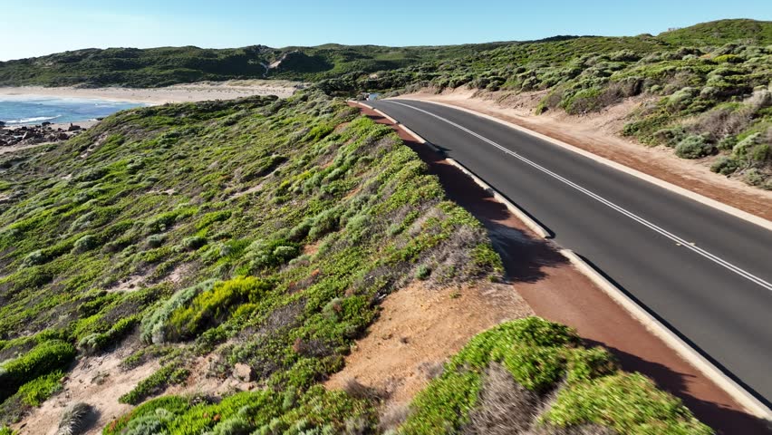Drone footage of the lush greenery and winding road leading to Surfers Point, Margaret River, Western Australia, with ocean waves breaking at the iconic coastline.