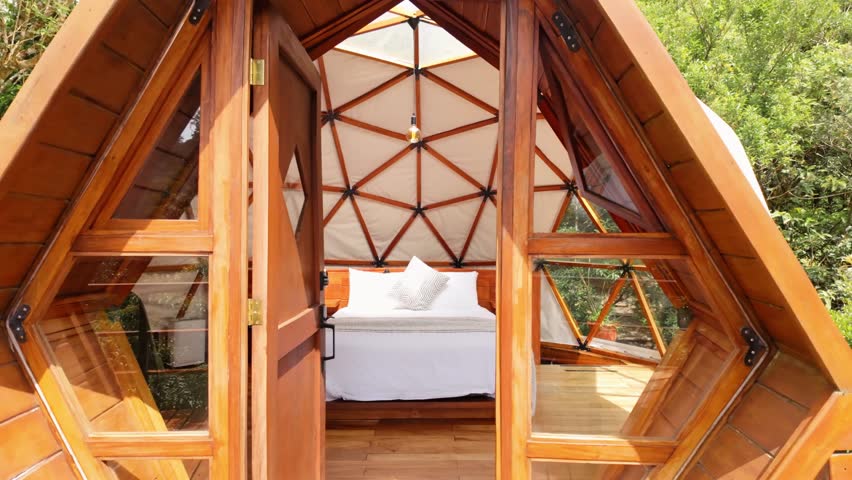 Dolly shot moving into a cozy and modern bedroom inside a geodesic dome glamping tent in the forest