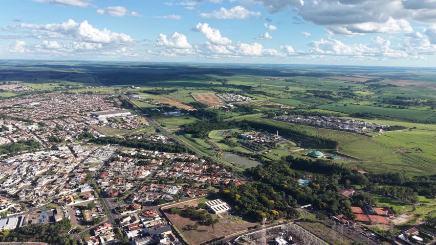 This video shows an aerial view of a city surrounded by lush green fields and a blue sky with clouds. The footage captures the urban landscape and natural scenery, showcasing the contrast between the built environment and the natural world.
