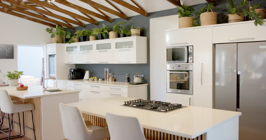 Camera is starting to pan left across white kitchen island with gas cooktop, showing full layout. Contemporary, openplan, neutral, daylight, warm, spacious, home