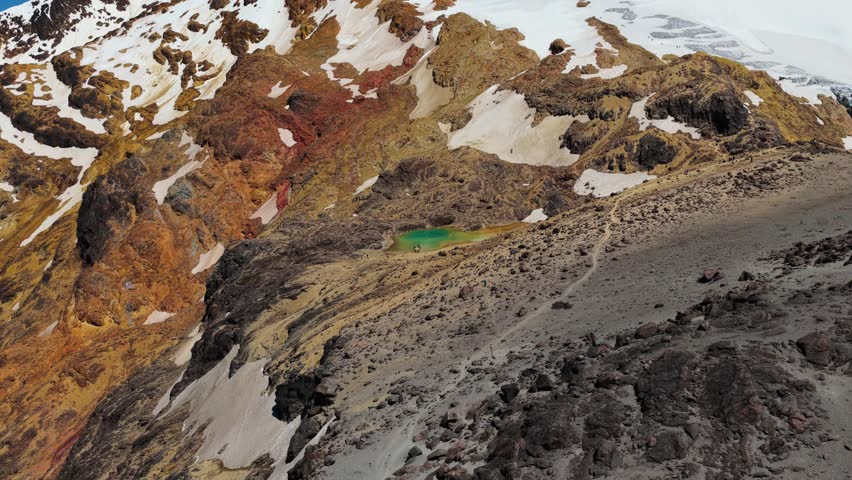 Aerial drone view of Laguna Verde, a small turquoise crater lake on the slopes of Cayambe volcano in the Ecuadorian Andes, surrounded by rugged volcanic terrain and high altitude landscape.