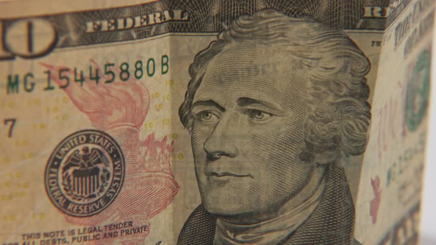 Alexander Hamilton the first U.S. Secretary of the Treasury portrait on printed ten 10 dollar bill of United States of America cash and printed treasury bills in close up and studio slo mo slow motion