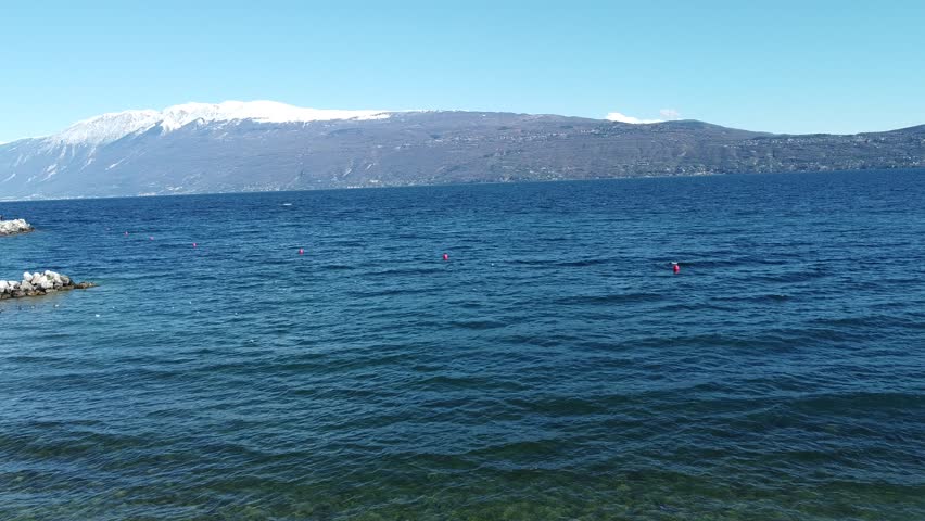 Pebble beach in Toscolano Maderno on Lake Garda with snow-capped mountains.