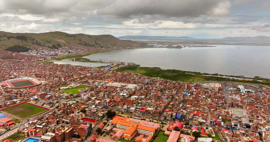 Urban sprawl and waterfront of Puno city along the bay of Lake Titicaca in Peru. Aerial forward